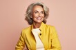 Portrait of a smiling senior business woman in yellow jacket on pink background.