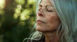 Innere Ruhe: Eine ältere Frau mit geschlossenen Augen atmet tief in der Natur ein.