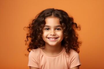 Portrait of a smiling little girl with curly hair over orange background