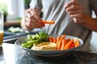 © SazzadurRahaman - Young man eating carrot stick with hummus dip on the kitchen. Hummus served with raw vegetables on the plate generative ai