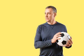 Poster - Portrait of sporty middle-aged man with soccer ball on yellow background