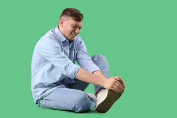 Wall Mural - Young man suffering from foot pain on green background