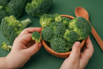 Wall Mural - Broccoli in the hands of a child on a green background