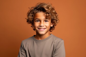 Wall Mural - Portrait of a smiling little boy with curly hair on brown background