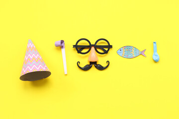 Sticker - Funny glasses with paper fish party hat and whistle on yellow background. April Fools Day celebration