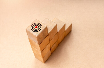 Wall Mural - Target dart icon on top of wooden blocks graph steps on brown kraft paper background, top view. Business target, growth process, profit, aim investment, objective goal, economic improvement concepts.