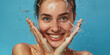 Beautiful smiling girl under splashes of water with fresh skin on a blue background. Concept of skin care, cleansing and moisturizing. Facial beauty