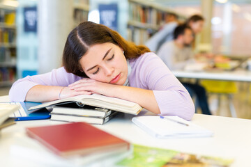 Canvas Print - Tired young woman lying on stack of books in public library