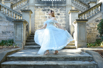 Wall Mural - portrait of beautiful female model wearing blue fantasy ballgown, like a fairytale elf princess. standing on staircase, walking up stairs of a romantic castle balcony location.
