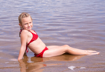 Wall Mural - A girl plays on a sandy beach on the shore of a lake in the summer heat.