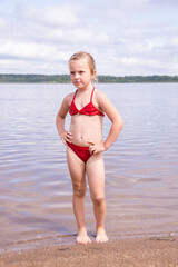 Wall Mural - A girl plays on a sandy beach on the shore of a lake in the summer heat.