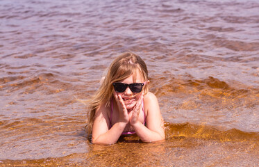 Wall Mural - A girl plays on a sandy beach on the shore of a lake in the summer heat.