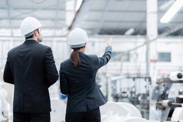 Back photo of 2 male American engineers and female architect in the plastic and steel manufacturing industry. Point to the goals of the company's business project. Around there are machines working.