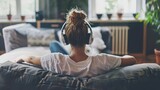 Fototapeta Miasto - Relaxed young woman listening to music with headphones while lying on sofa at home