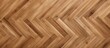 A close up of a hardwood floor in a herringbone pattern, showcasing the warm brown hues of the wood stain and varnish. The beige planks create a visually appealing design