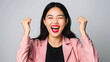 Portrait of a happy young beautiful Asian fashionable woman celebrating success on light gray background, 