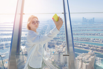 Wall Mural - Tourist young woman make selfie photo on phone on background skyscrapers of Dubai UAE with sunlight