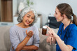 © NanSan - Caucasian female doctor introduces medicine to an elderly Asian patient while seated on a sofa, providing guidance and information about the prescribed medication.