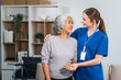 © NanSan - Caucasian female doctor assists in supporting an elderly Asian patient while they both sit on the sofa, ensuring comfort and stability during the interaction.
