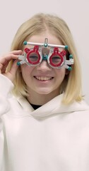 Wall Mural - vertical portrait happy little girl patient ophthalmology clinic, vision test in progress cheerful child trying on trial frames during an optometric examination for accurate eyeglass fitting