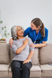 © NanSan - A Caucasian female doctor provides encouragement and advice on maintaining good health to an elderly Asian patient while they sit together on the sofa.