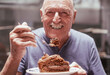 © luciano - Portrait of senior man smiling while enjoying a break with a slice of chocolate cake. Greedy and happy old man holding fork with a piece of cake