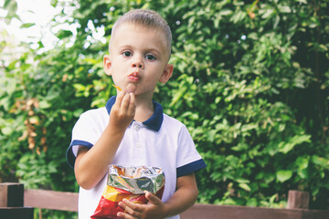 Wall Mural - a child eats chips from a pack on the background of nature