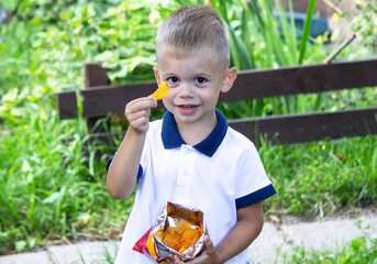 Wall Mural - a child eats chips from a pack on the background of nature.