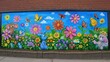 Mural na ścianie budynku przedstawia radosną scenę  wiosenną dla dzieci z kolorowymi kwiatami i zwierzątkami
