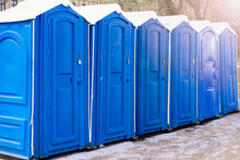 Row Of Blue Clean Outdoor Portable Toilets In Winter With Bright Blue Doors And White Roof At Urban Street