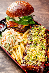 Poster - A sumptuous meal awaits: a gourmet burger, ribs, fries, coleslaw, and grilled corn on a dark wooden table