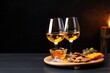 Two glasses of golden wine paired with cheese, grapes, and crackers on a round wooden board, set against a dark, moody backdrop. Elegant Evening Wine Tasting with Appetizers