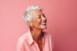 Portrait of happy senior woman with short white hair laughing against pink background