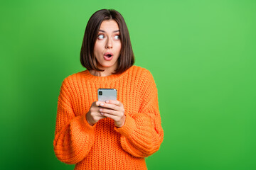 Wall Mural - Portrait of impressed crazy lady hold smart phone open mouth look empty space isolated on green color background