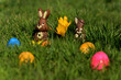 Schokoladen Osterhasen sitzen im grünen Gras, umgeben von bunten Ostereier und blühenden Frühlingsblumen
