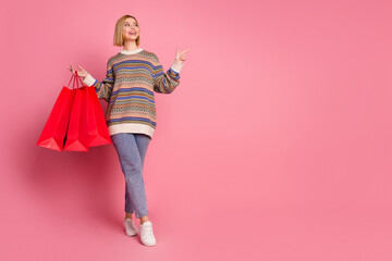 Wall Mural - Full size photo of nice girl wear ornament sweater hold shopping bags look directing at sale empty space isolated on pink color background