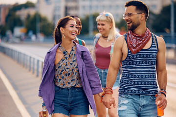 Wall Mural - Happy couple of festival goers holding hands while walking on street.