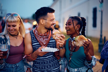 Wall Mural - Multiracial group of happy friends eating hamburgers and talking during summer music festival.