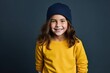 Smiling little girl in yellow sweater and blue cap over dark blue background
