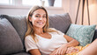 Relaxed Young Woman Smiling on a Comfortable Sofa in a Bright Living Room.