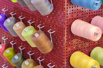 Aufkleber - A row of colorful spools of thread are displayed in a store. The spools are arranged in a rainbow pattern, with each color being represented in the display. The spools are of various sizes