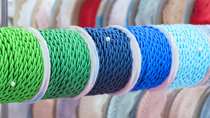 Aufkleber - A row of colorful spools of thread, tape, braid  are displayed in a store. The spools are arranged in a rainbow pattern, with each color being represented in the display. The spools various sizes
