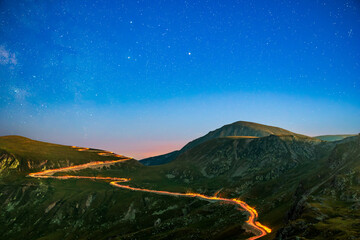Wall Mural - transalpina road under a starry night with traffic trails along the winding road. transalpina is one
