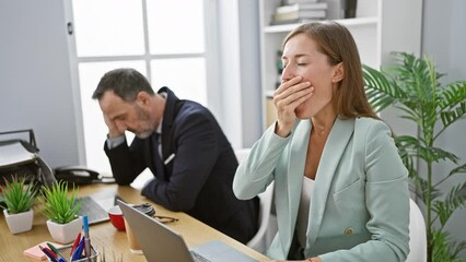 Wall Mural - Two exhausted business workers yawning together, signifying long hours of collaborative work at office