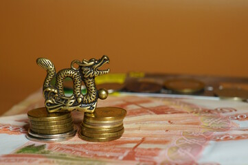 Wall Mural - A metal dragon statuette with coins and paper money. An economic symbol. Horoscope and Feng Shui.