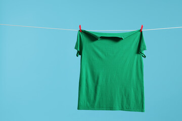 Canvas Print - One green t-shirt drying on washing line against light blue background. Space for text