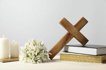 Burning church candles, wooden cross, ecclesiastical books and flowers on white table