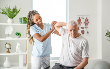 Wall Mural - Black physiotherapist helping senior man with in clinic. Elderly man undergoing physiotherapy treatment for injury