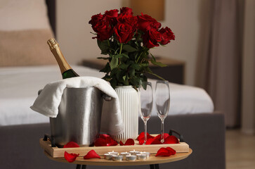 Poster - Honeymoon. Sparkling wine, glasses and bouquet of roses on wooden table in room