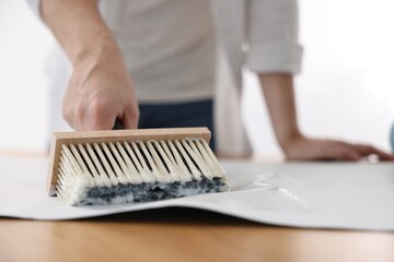 Wall Mural - Man applying glue onto wallpaper sheet at table indoors, closeup